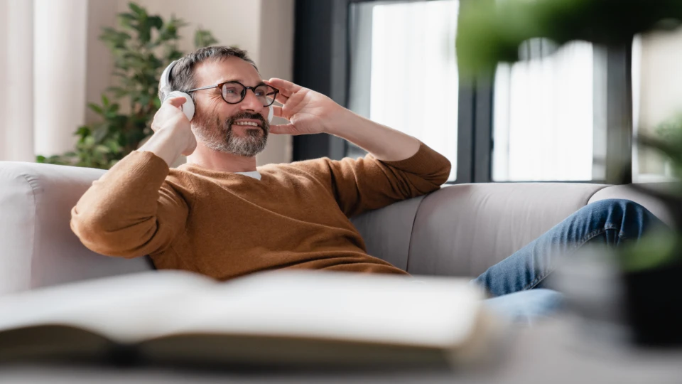 Ein Mann mittleren Alters hört entspannt einen Podcast auf einer Couch sitzend