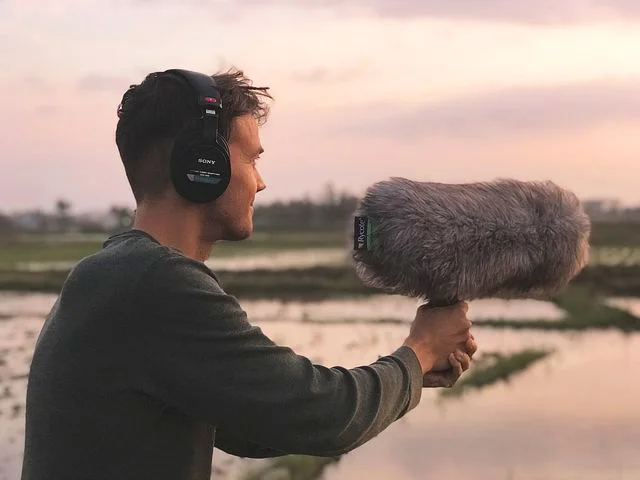 Ein junger Mann nimmt eine Field Recording Tonaufnahme mit einem in der Hand gehaltenen Mikrofon mit Windschutz vor